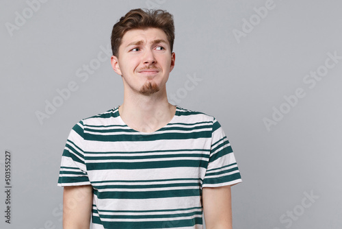 Young stressed depressed sad displeased worried dissatisfied man 20s wear blue striped t-shirt look aside on worspace area mock up isolated on plain gray background studio. People lifestyle concept. photo