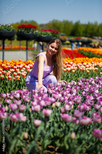 A young woman in a pink suit stands in a blooming field of tulips. Spring time © Дмитрий Ткачук