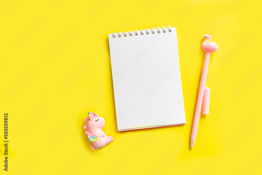 Unicorn. Blank white notepad on a spiral with a pink pen. Top view with copy space, flat lay on yellow background Unicorn. Blank white notepad on a spiral with a pink pen. Top view with copy space, flat lay on yellow background