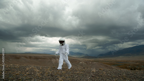 An astronaut explores an unknown planet. Heavy cloudy sky.