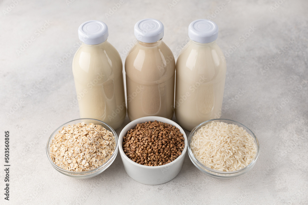 Bottles with vegetable milk: oatmeal, buckwheat and rice with ingredients on a light background Bottles with vegetable milk: oatmeal, buckwheat and rice with ingredients on a light background
