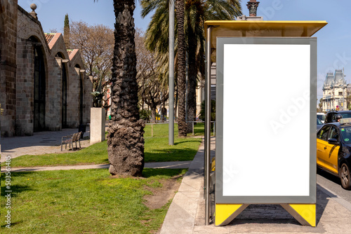 Bus stop mockup in Europe. Vertical empty blank white poster or billboard in the city street. Mock up. Street poster next to road. Sunny summer day.