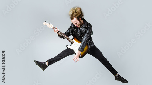 Brutal bearded man jumping with electric guitar. Rock musician. Heavy metal player. Music star. photo