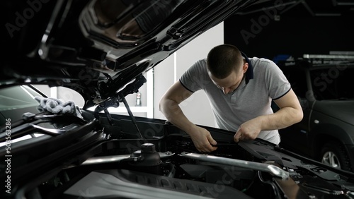 Repairman - auto mechanic, works in a car repair shop. Installation of parts under the hood. The master installs rubber bands under the hood of the car.