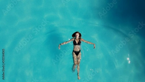 Beautiful girl in a swimsuit swims on his back in the pool top view. Taken from a drone