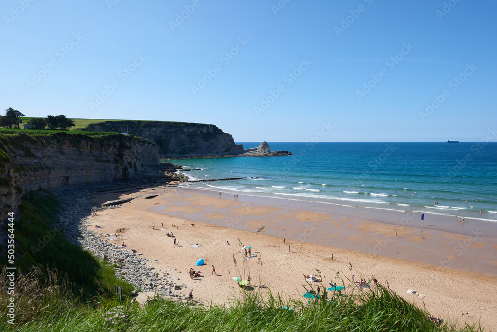 A beach surrounded by cliffs and vegetation under a clear sky.