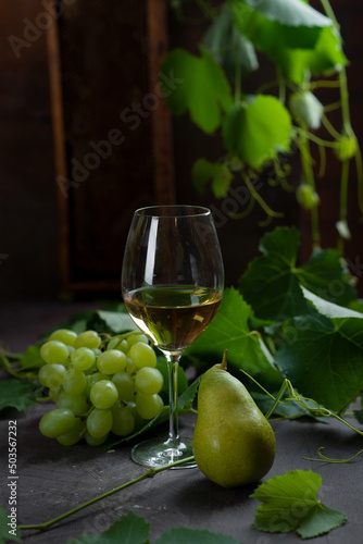 grape leaves and bunches of white grapes with a glass of white wine on a table in the cellar