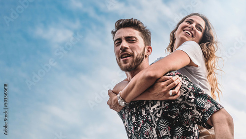 Couple of young people carefree piggybacking against the sky in the summer - life style concept of friends relationship and young people chill out bonding - focus on the woman face
