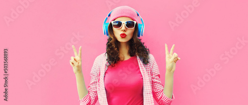 Summer colorful portrait of stylish modern young woman listening to music in headphones posing on pink background
