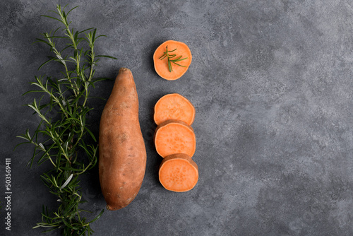 Raw whole orange sweet potato and slices of batatas with fresh rosemary on grey concrete background, top view, copy space, flat lay photo