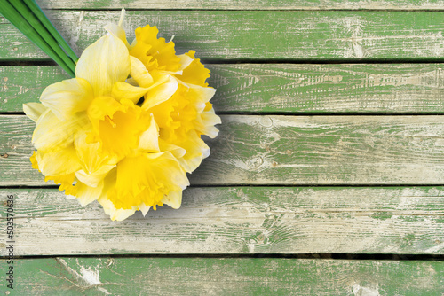 Bouquet of yellow daffodils, narcissus on green wooden background with copy space. Mockup, template for holiday, birthday, mother's day on yellow background. Top view, flat lay with copy space