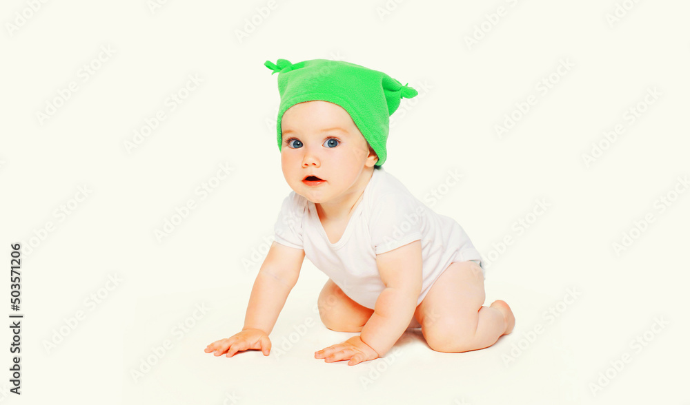 Portrait close up of cute baby crawling on the floor wearing green winter knitted hat on white background Portrait close up of cute baby crawling on the floor wearing green winter knitted hat on white background