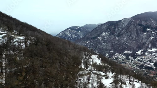 Flying above the swiss alps in the winter.  Bare trees and the snow show the season.  Grey, snowy skies over the mountains.  photo