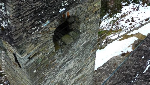 Flying above the swiss alps in the winter.  A closeup of an old church's bell tower.  Bare trees and the snow show the season.  Grey, snowy skies over the mountains.  photo