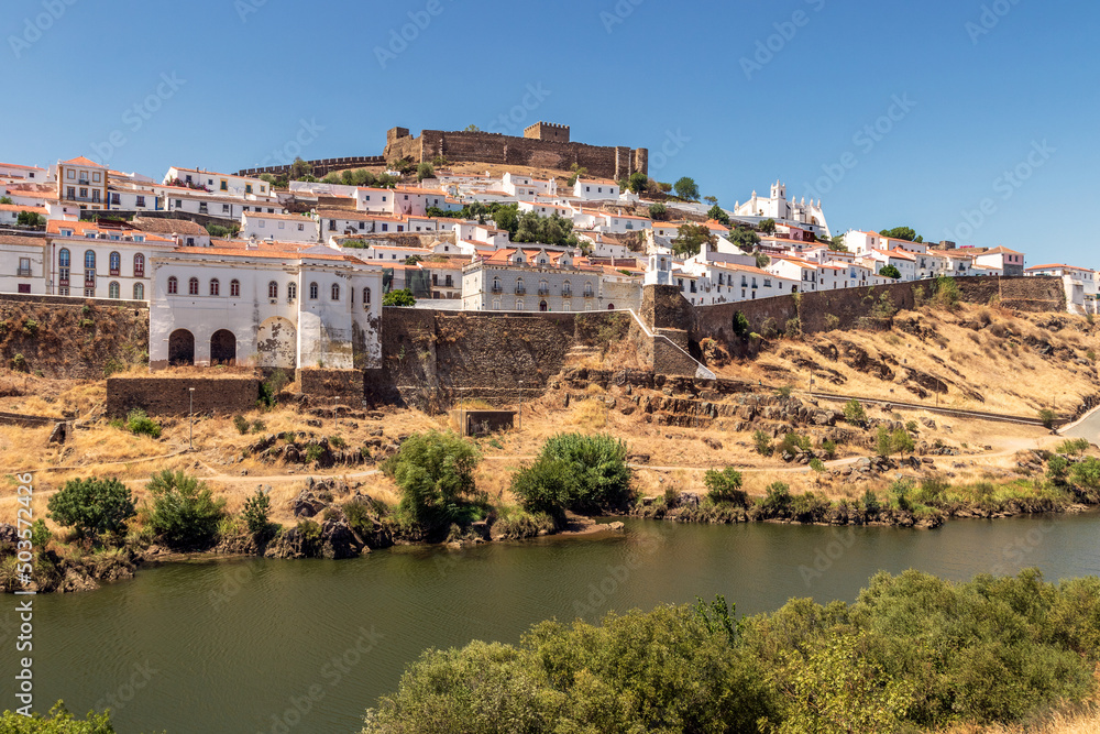 View of the village of Mértola in Portugal, with the Guadiana river in the foreground, on a sunny day in summer.