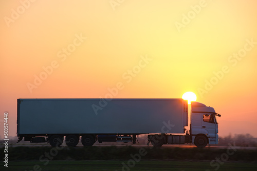 Semi-truck with cargo trailer driving on highway hauling goods in evening. Delivery transportation and logistics concept