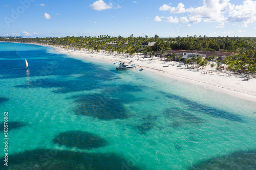 Fototapeta Naklejka Na Ścianę i Meble -  Tropical coastline with resorts, palm trees and caribbean sea with floating boats. Dominican Republic. Aerial view