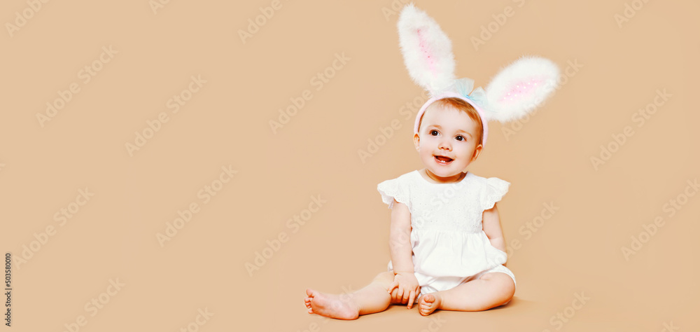 Portrait of cute baby with rabbit ears sitting on brown background Portrait of cute baby with rabbit ears sitting on brown background