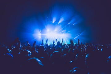 A crowded concert hall with scene stage lights in blue tones, rock show performance, with people silhouette, on dance floor air during a concert festival