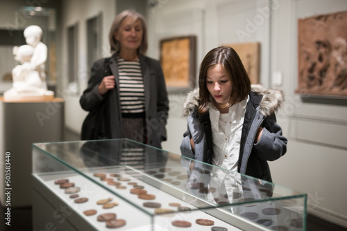 Portrait of interested cheerful preteen girl looking at exposition in historical museum..