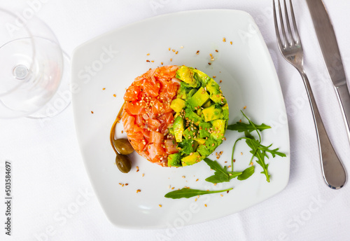 Delicious seafood tartare made of raw salmon, onion and avocado served with arugula and capers photo