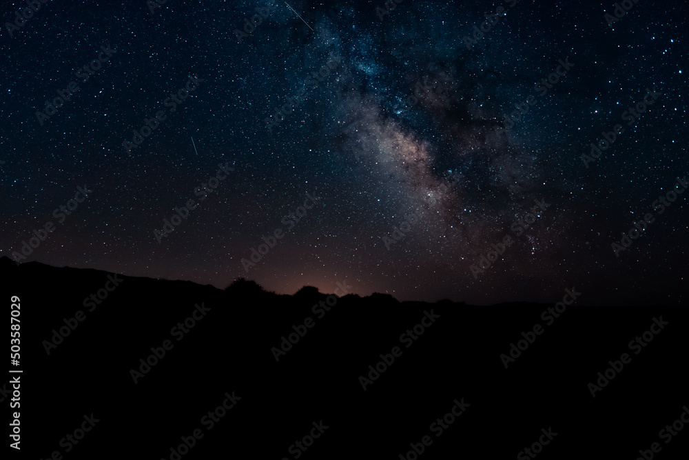 The Milky Way galaxy over the landscape in silhouette The Milky Way galaxy over the landscape in silhouette