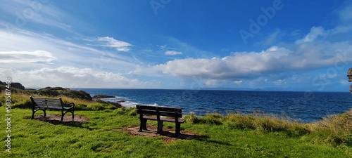Fotografering Beautiful landscape of a seaside with wooden benches and green grass in Scotland