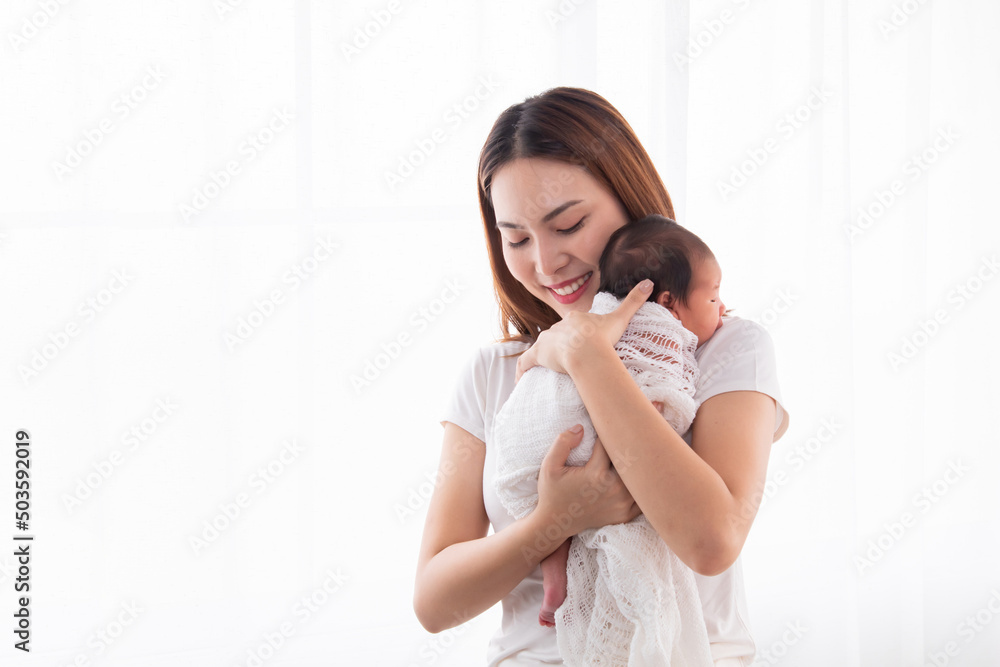 Beautiful aisan mother holding and embrace newborn baby in her arms. Woman holding adorable infant in arms and support baby back by her hand. mom and son spend time together in white room. Beautiful aisan mother holding and embrace newborn baby in her arms. Woman holding adorable infant in arms and support baby back by her hand. mom and son spend time together in white room.