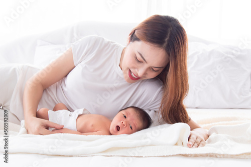 Beautiful asian mother and toddler lying in bedroom talking or singing together. Singlemom watching her son with love and tender. Mom playing with cute newborn baby and spend time together on bed.