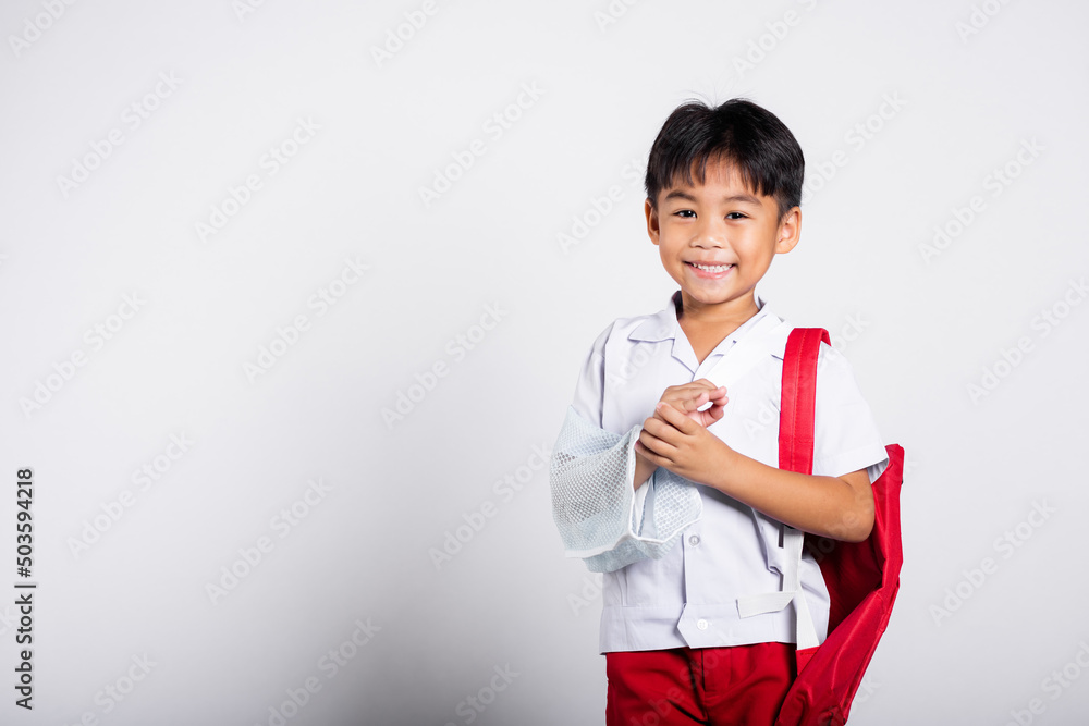 Asian student kid boy wearing student thai uniform accident broken bone wearing splint arm plaster fiberglass cast covering arm in cast at studio shot isolated on white background, back to school Asian student kid boy wearing student thai uniform accident broken bone wearing splint arm plaster fiberglass cast covering arm in cast at studio shot isolated on white background, back to school