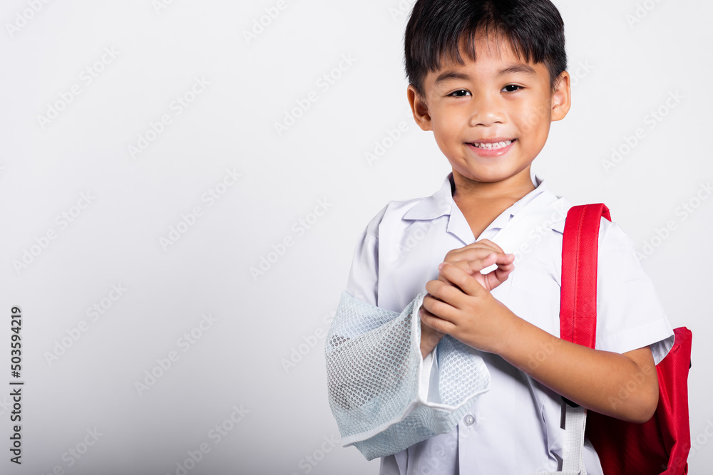 Asian student kid boy wearing student thai uniform accident broken bone wearing splint arm plaster fiberglass cast covering arm in cast at studio shot isolated on white background, back to school Asian student kid boy wearing student thai uniform accident broken bone wearing splint arm plaster fiberglass cast covering arm in cast at studio shot isolated on white background, back to school