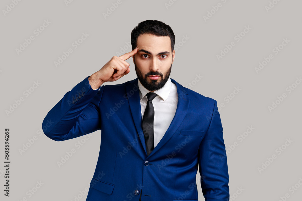 Unhappy frustrated bearded man showing stupid gesture, does not believe in his strengths, capabilities, disappointed, wearing official style suit. Indoor studio shot isolated on gray background. Unhappy frustrated bearded man showing stupid gesture, does not believe in his strengths, capabilities, disappointed, wearing official style suit. Indoor studio shot isolated on gray background.