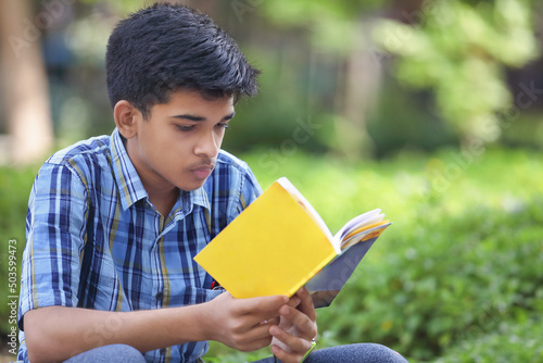 Indian teenage boy reading book in park	
 photo