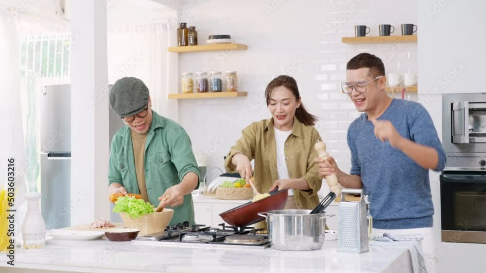 Asian people friends enjoy cooking pasta in cooking pan with talking together in the kitchen at home. Man and woman having dinner party meeting celebration eating food together on holiday vacation Asian people friends enjoy cooking pasta in cooking pan with talking together in the kitchen at home. Man and woman having dinner party meeting celebration eating food together on holiday vacation