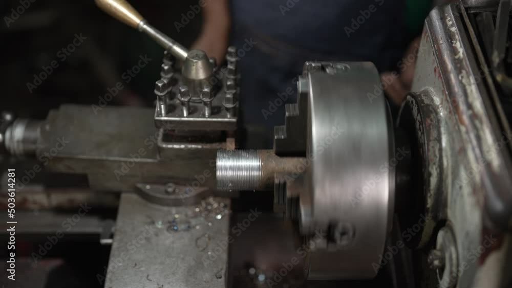 4K 50fps, Close-up of the iron plugged into the lathe, rotating according to the work of the lathe, which is working now, with an senior mechanic operating this lathe inside his small factory. 4K 50fps, Close-up of the iron plugged into the lathe, rotating according to the work of the lathe, which is working now, with an senior mechanic operating this lathe inside his small factory.