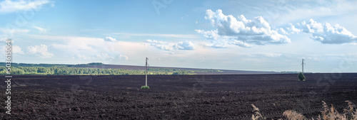 panorama of a lot of black fertile plowed soil against a background of blue sky