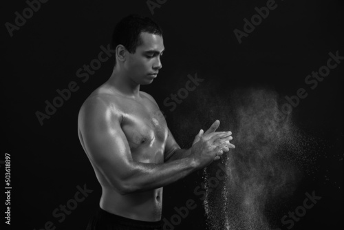 Black and white portrait of sporty African-American man applying talc powder on hands against dark background