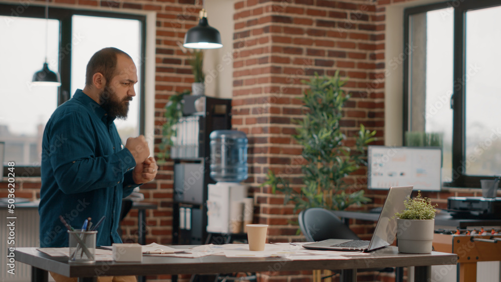 Employee celebrating successful business achievement after reading good news on laptop. Satisfied man enjoying victory and celebration, showing excitement and feeling happy in office.