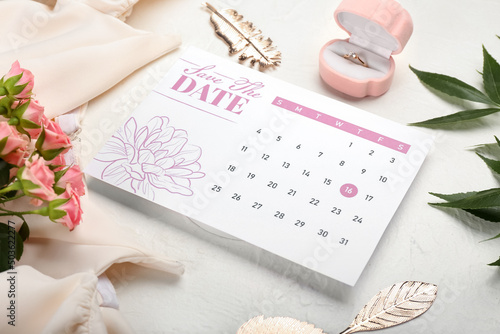 Wedding calendar with marked date, box with engagement ring and beautiful flowers on light table