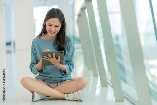 Free Download asian female collage young campus woman sitting on the mall floor using tablet browing surf data online social media with cheerful fun smiling,asian woman digital nomad sit on floor casual work online - GFXLoad