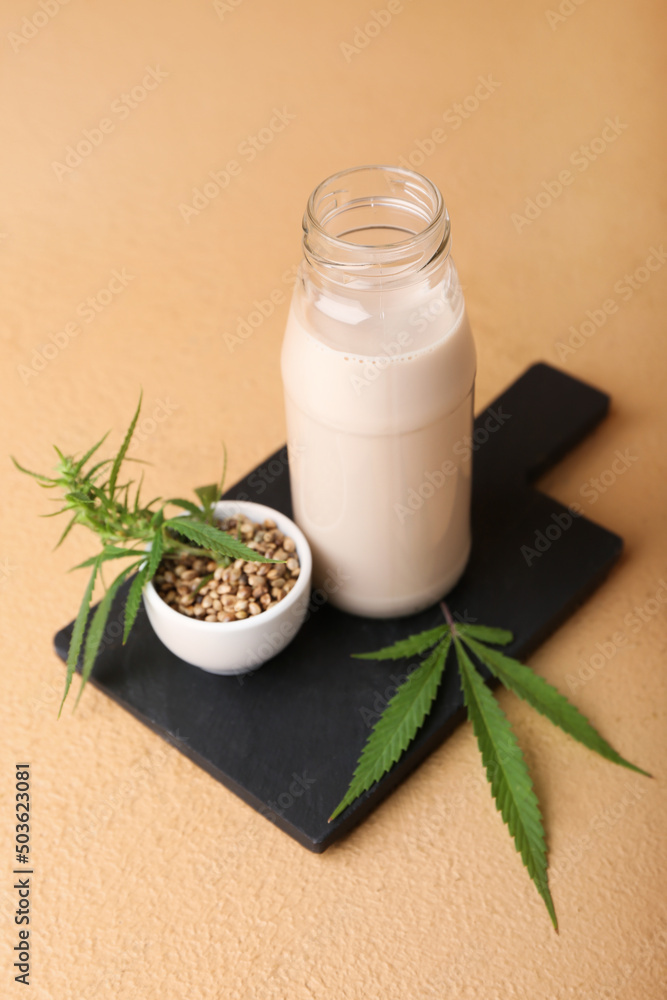 Board with bottle of hemp milk and seeds on color background Board with bottle of hemp milk and seeds on color background