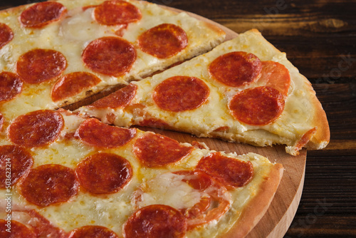 Pepperoni pizza cut into pieces with salami and cheese on a wooden background close-up. Horizontal orientation, no people