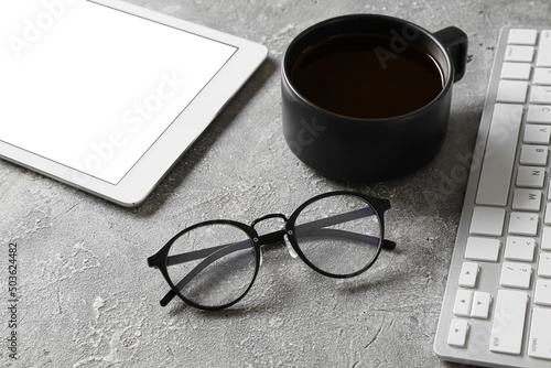 Eyeglasses, cup of coffee, tablet computer with keyboard on grey background, closeup