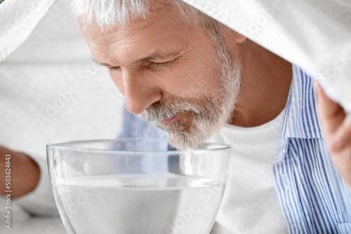 Mature man doing steam inhalation at home, closeup