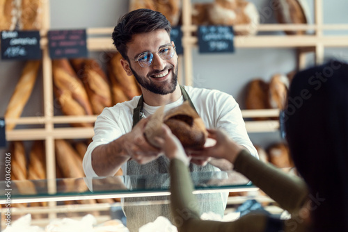 Cheerful seller giving fresh loaf of bread to smiling woman in the pastry shop Fototapet