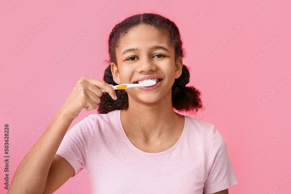 African-American teenage girl brushing teeth on pink background African-American teenage girl brushing teeth on pink background