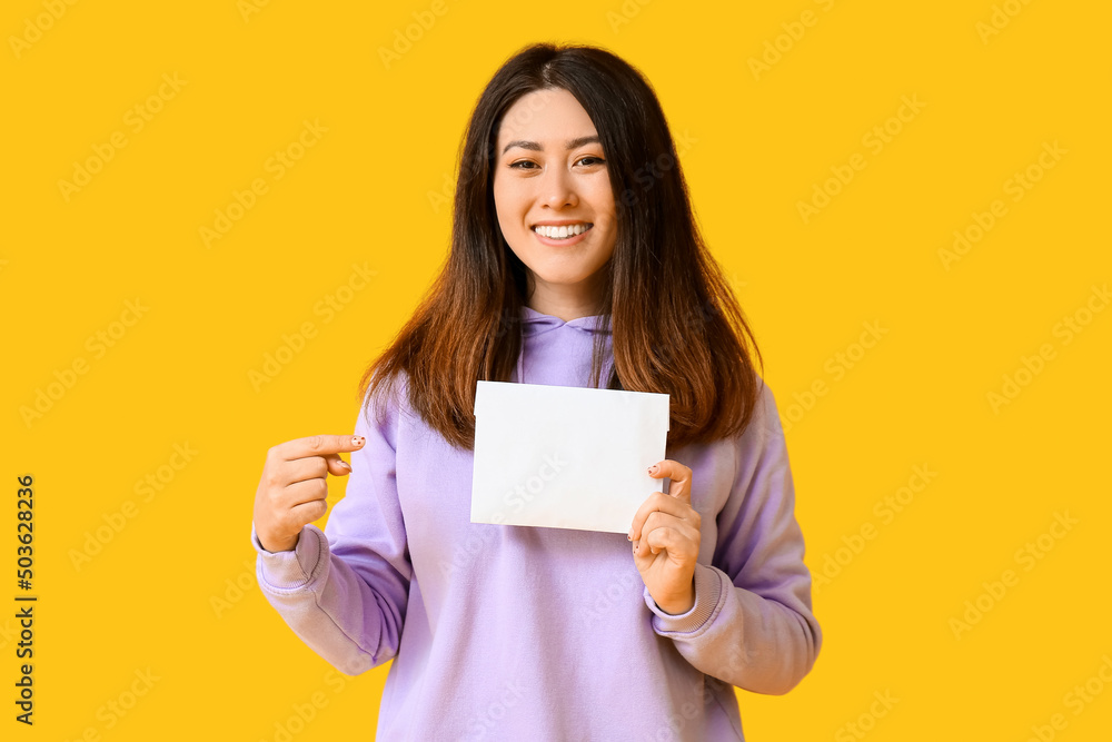 Young Asian woman pointing at invitation on yellow background Young Asian woman pointing at invitation on yellow background