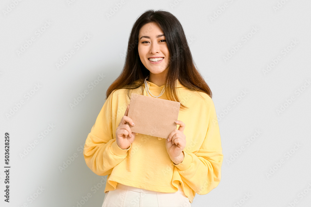 Young Asian woman with invitation on light background Young Asian woman with invitation on light background