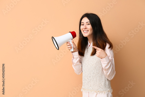 Young Asian woman with megaphone pointing at something on beige background