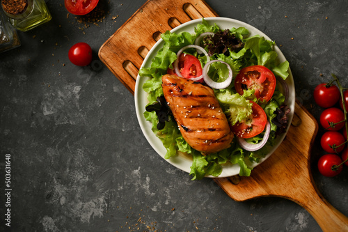 Fotografia Grilled chicken breast with fresh salad vegetables on a grey background
